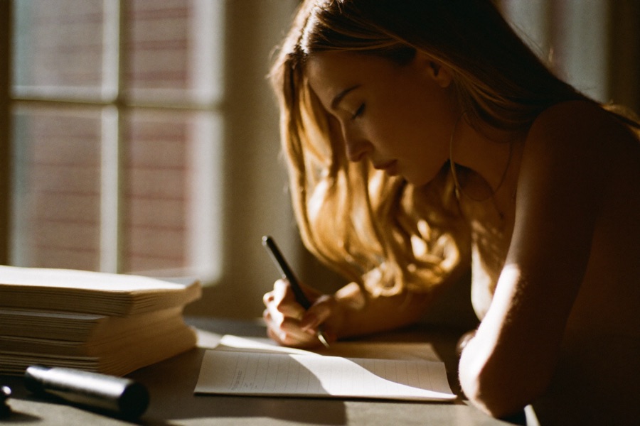 An author writing by hand in a notebook at a sunlit desk